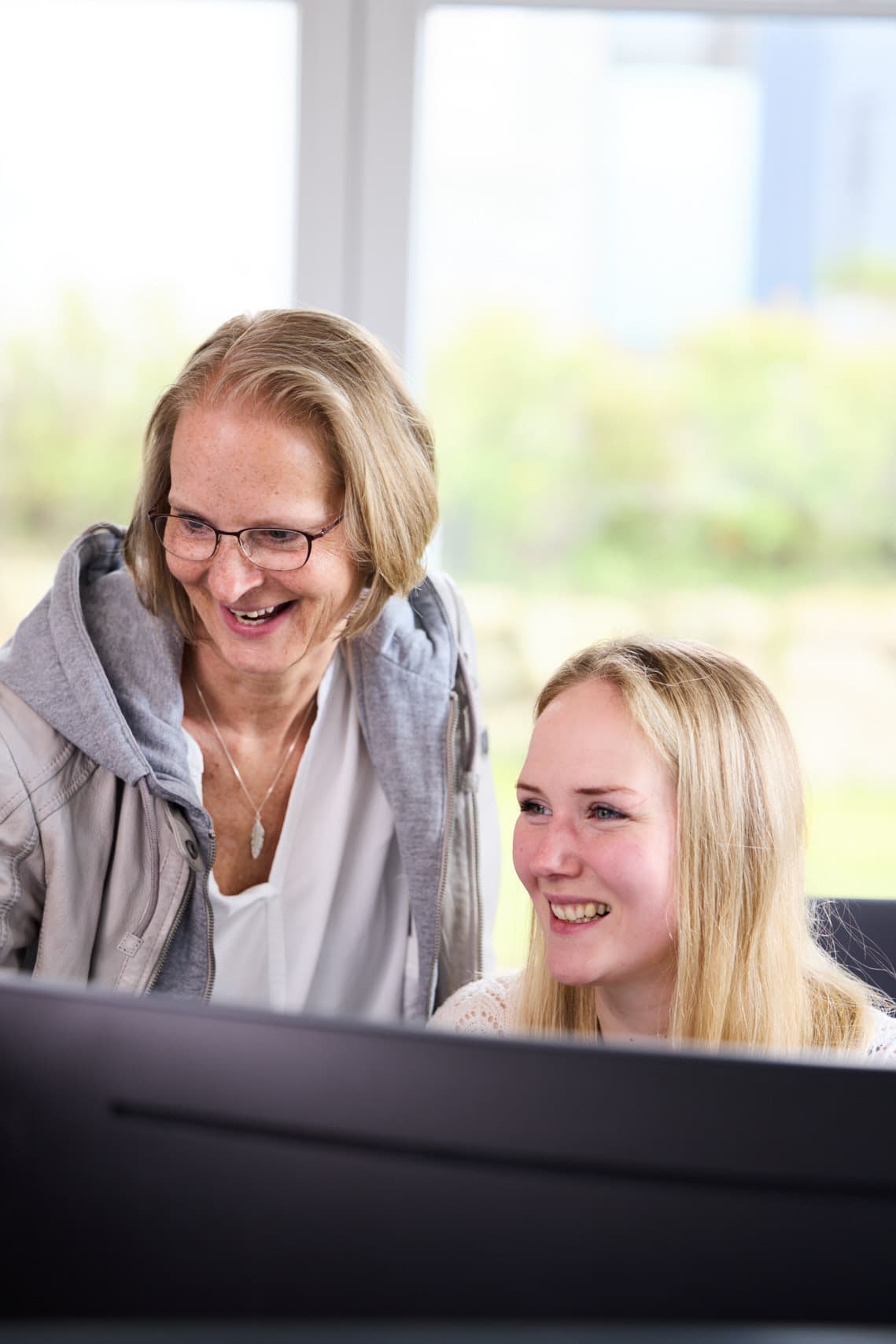 Zwei Kolleginnen lachen gemeinsam am Bildschirm